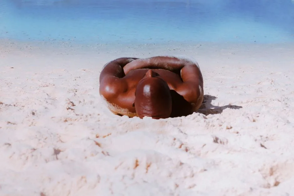 A deeply tanned man lying face down in white beach sand