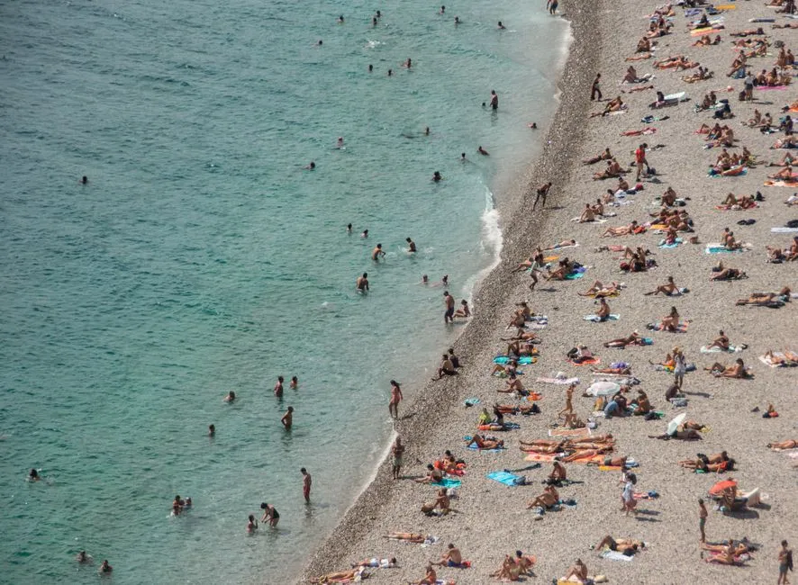 Aerial view of a packed beach, hundreds of people lying in the sun